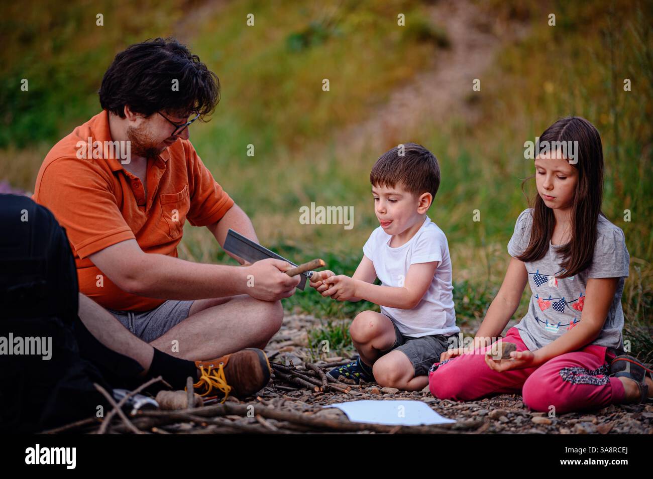 A father teaches his children how to use a saw and gather sticks during an outdoor activity. A hands-on learning experience promoting teamwork, skill- Stock Photo