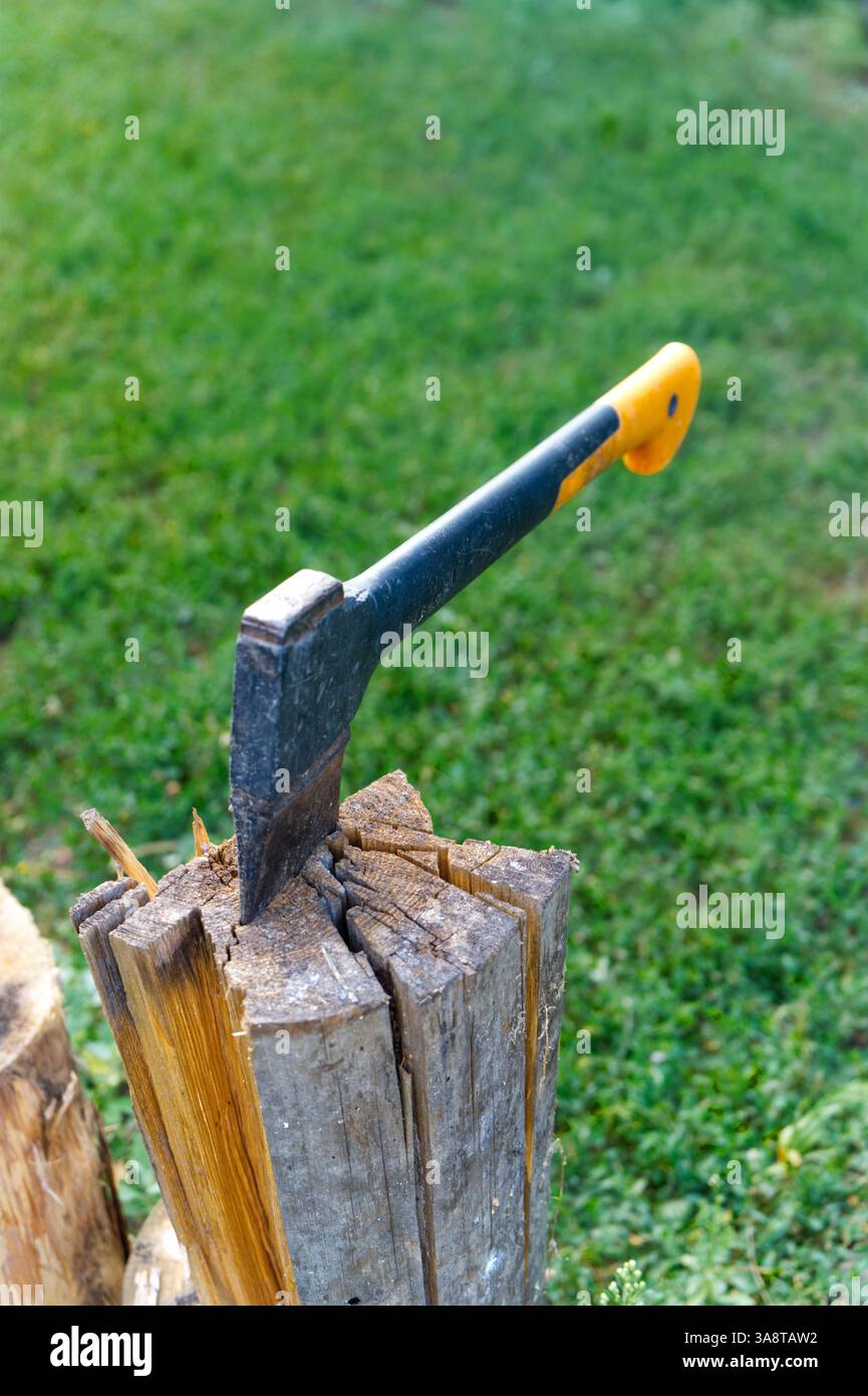 An axe with a yellow handle is embedded in a split log, set against a background of green grass. Stock Photo