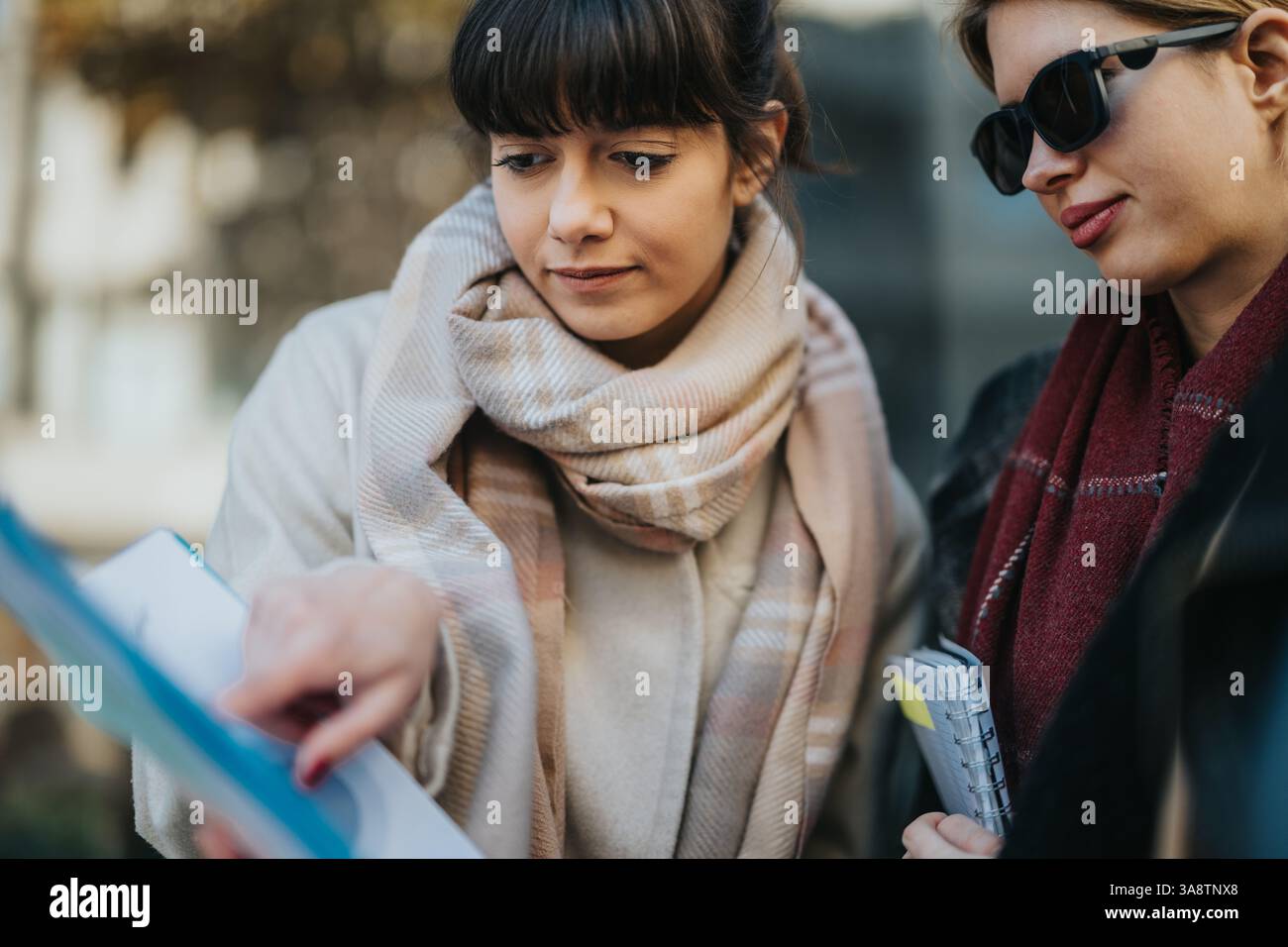 Two women reviewing documents outdoors while discussing and collaborating Stock Photo