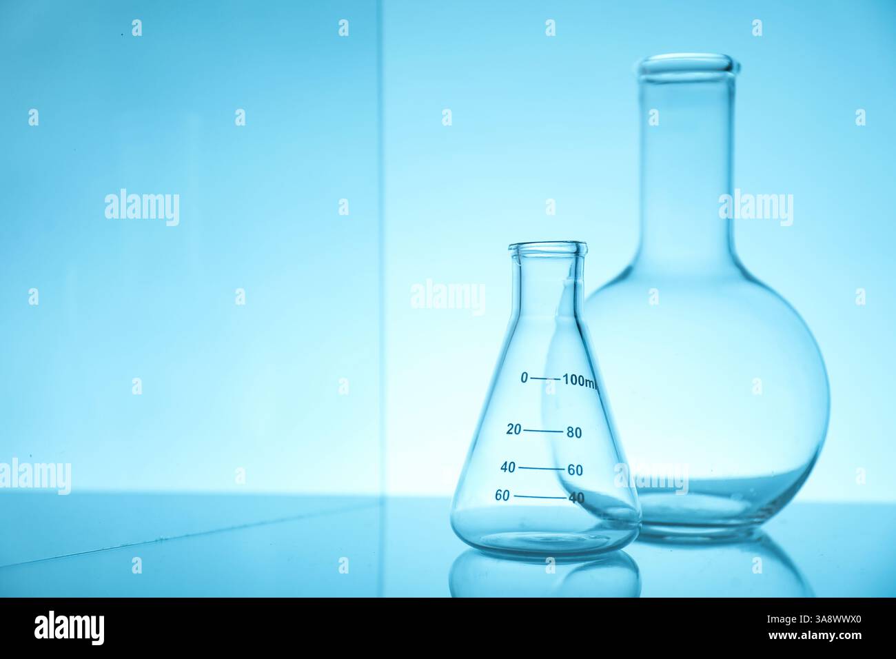 Empty flasks on mirror surface against light blue background, space for ...