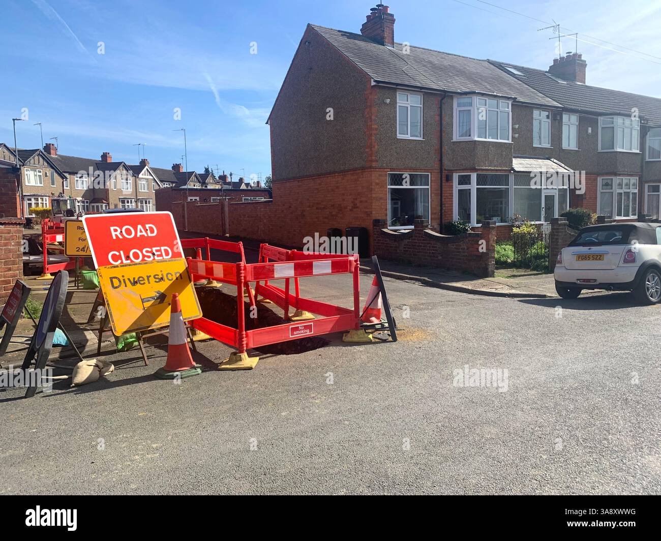 Road works in Northampton England UK Gas leak leaking dig digger wall house houses sign bollard bollards local place parked mini convertible hole in - Smartphone Captured Stock Image