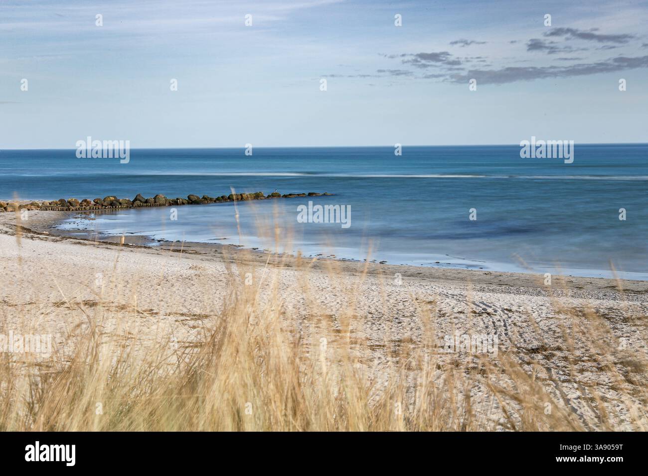 A beach with a rocky shoreline and a calm Baltic sea. The sky is clear and blue, and the water is a deep blue color. The beach is mostly empty, with o Stock Photo