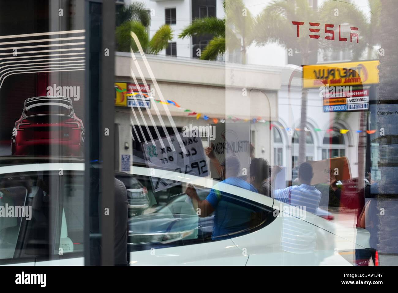 Protesters are seen reflected in the window of a Tesla dealership as ...