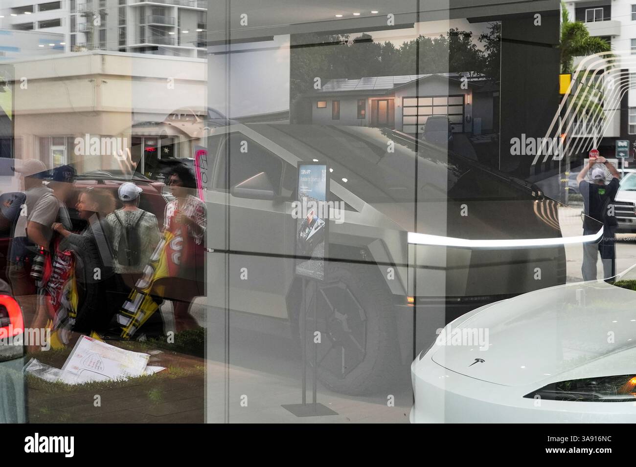 Protesters are seen reflected in the window of a Tesla dealership as ...