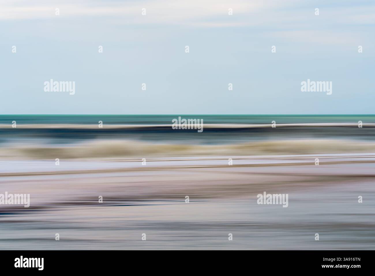 Blurred waves roll gently beneath a soft blue sky. Stock Photo