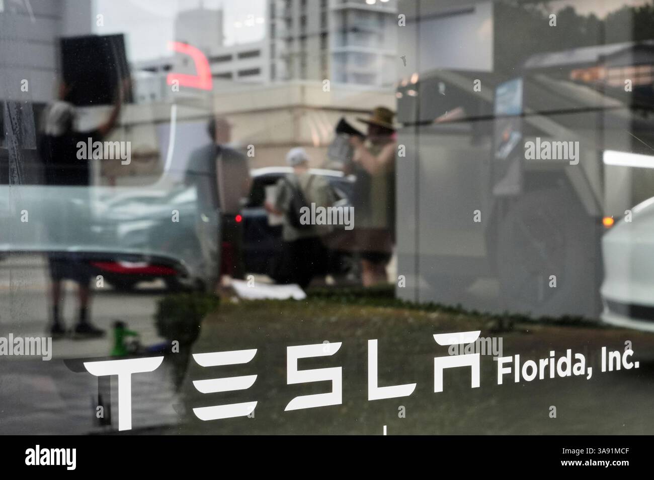 Protesters are reflected in the window of a Tesla dealership as they ...