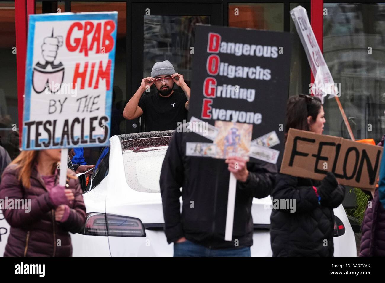 A Tesla worker watches as people wave signs during a protest against ...