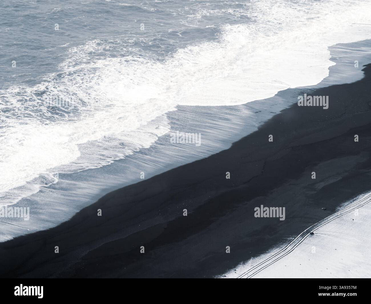 Aerial view of Dyrhólaey black beach in Iceland, where waves meet volcanic sand and fresh snow. Abstract winter coastal landscape with bold contrast a Stock Photo