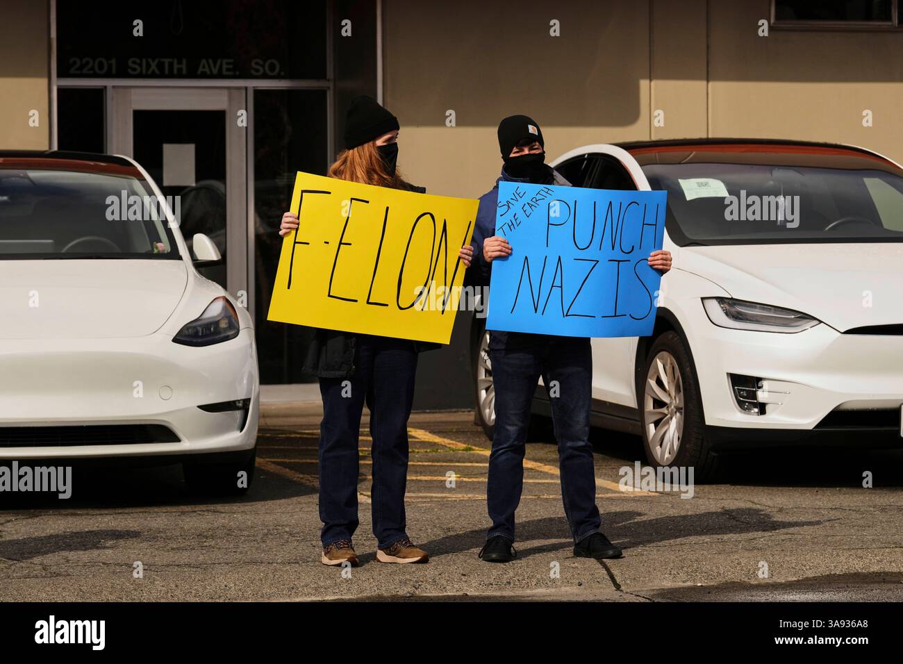 People hold signs in front of Tesla vehicles during a protest against ...