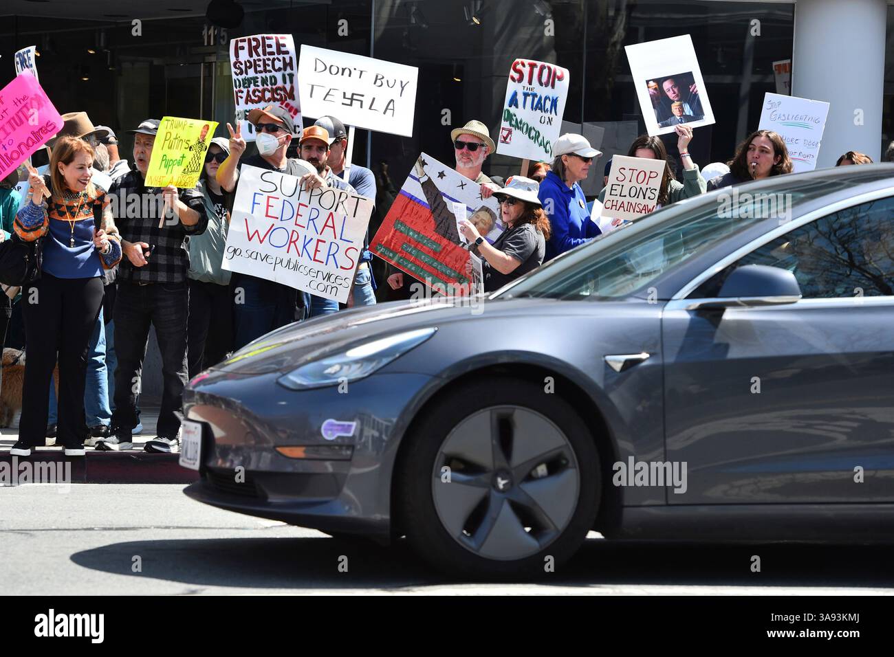 A Tesla driver stops at a stoplight as protesters hold signs in Walnut ...