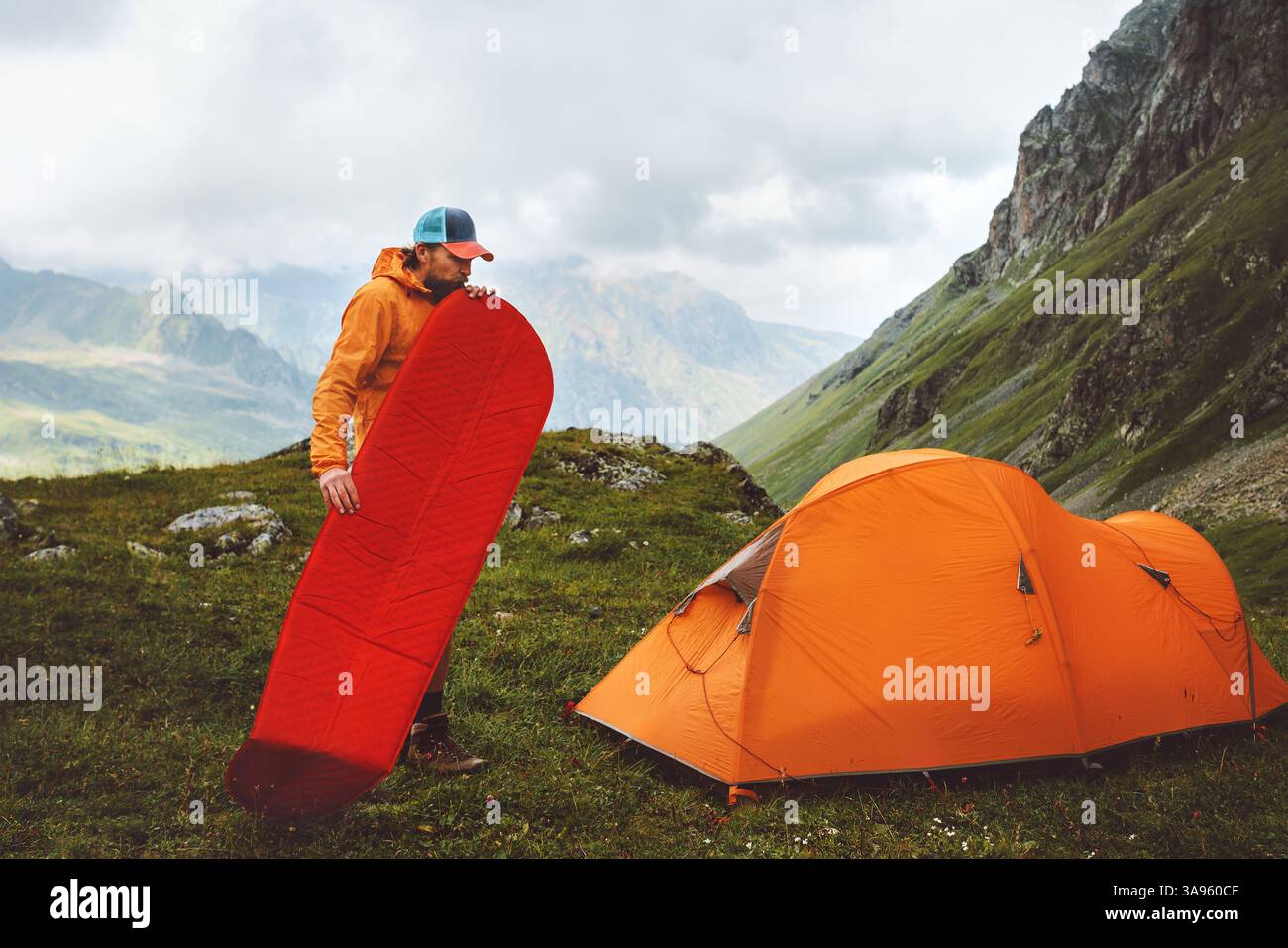 Camping in mountains: man traveling with sleeping pad and tent gear  adventure healthy lifestyle summer active vacations trip, hiker inflates mat clim Stock Photo