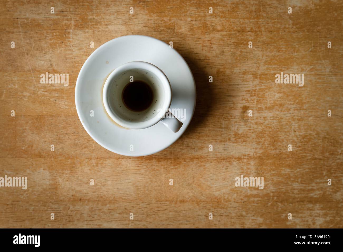 White ceramic espresso cup and saucer with dregs of coffee on an old brown wooden tabletop, from above. Stock Photo