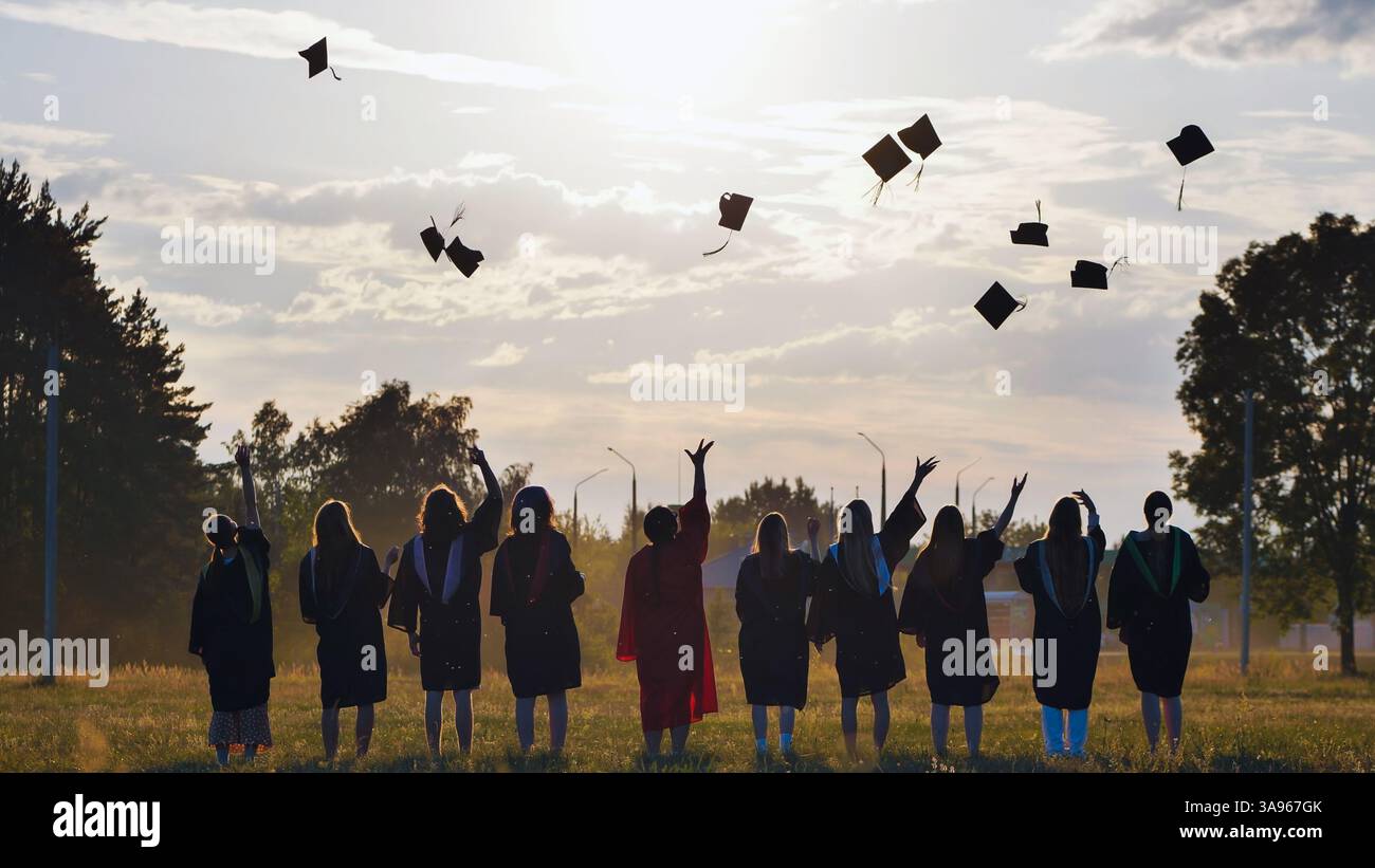 Students joyfully toss graduation caps into the air at sunset to ...