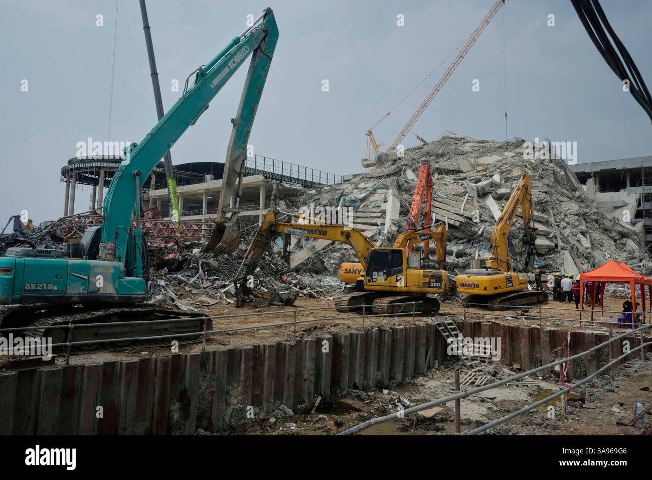 Heavy machineries clear the debris as rescuers work at the site of an ...