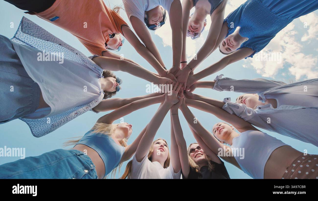School friends joining hands in a circle against a clear blue sky ...