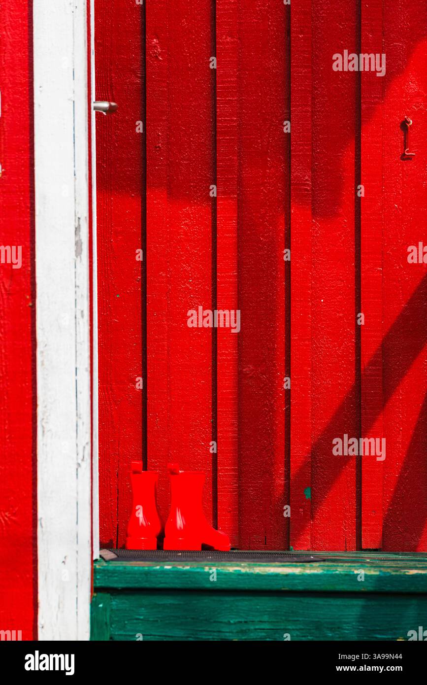 Bright red wooden planks create a striking background for vivid rubber boots, highlighting Gothenburg's unique architectural charm and playful color u Stock Photo