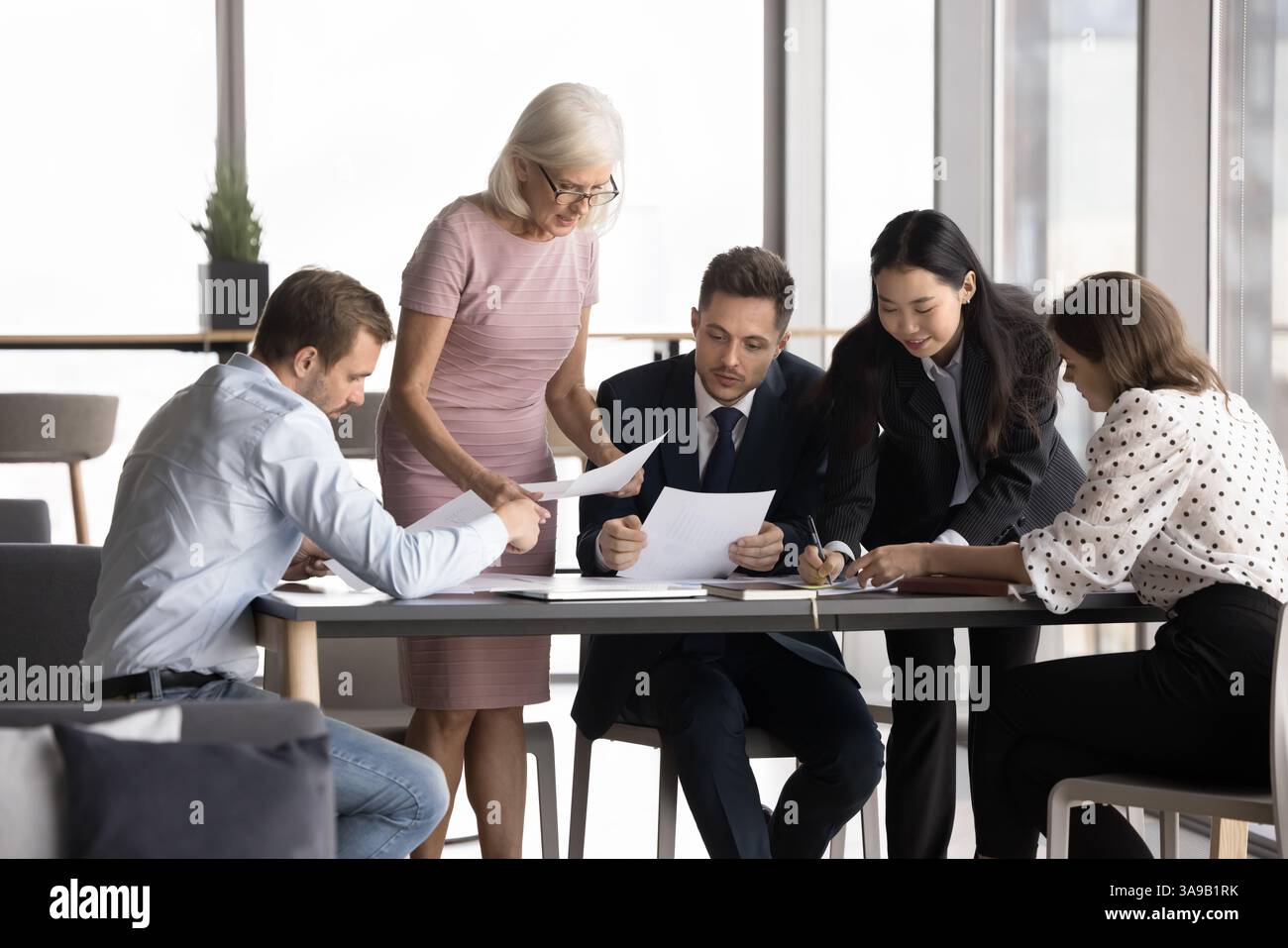 Business people discussing documents gathered around table Stock Photo