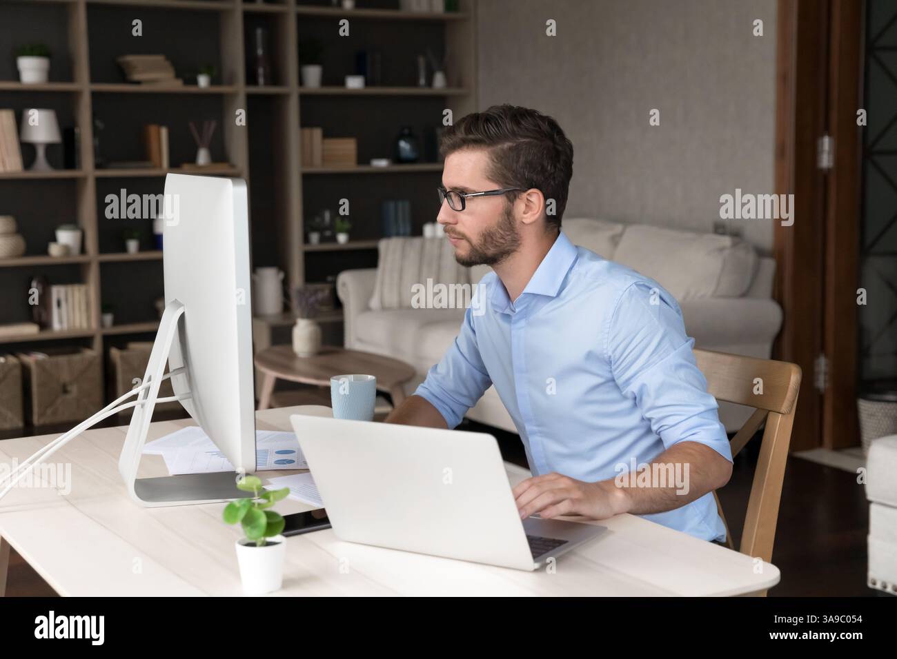 Young man freelancer using laptop and desktop computers at work Stock Photo