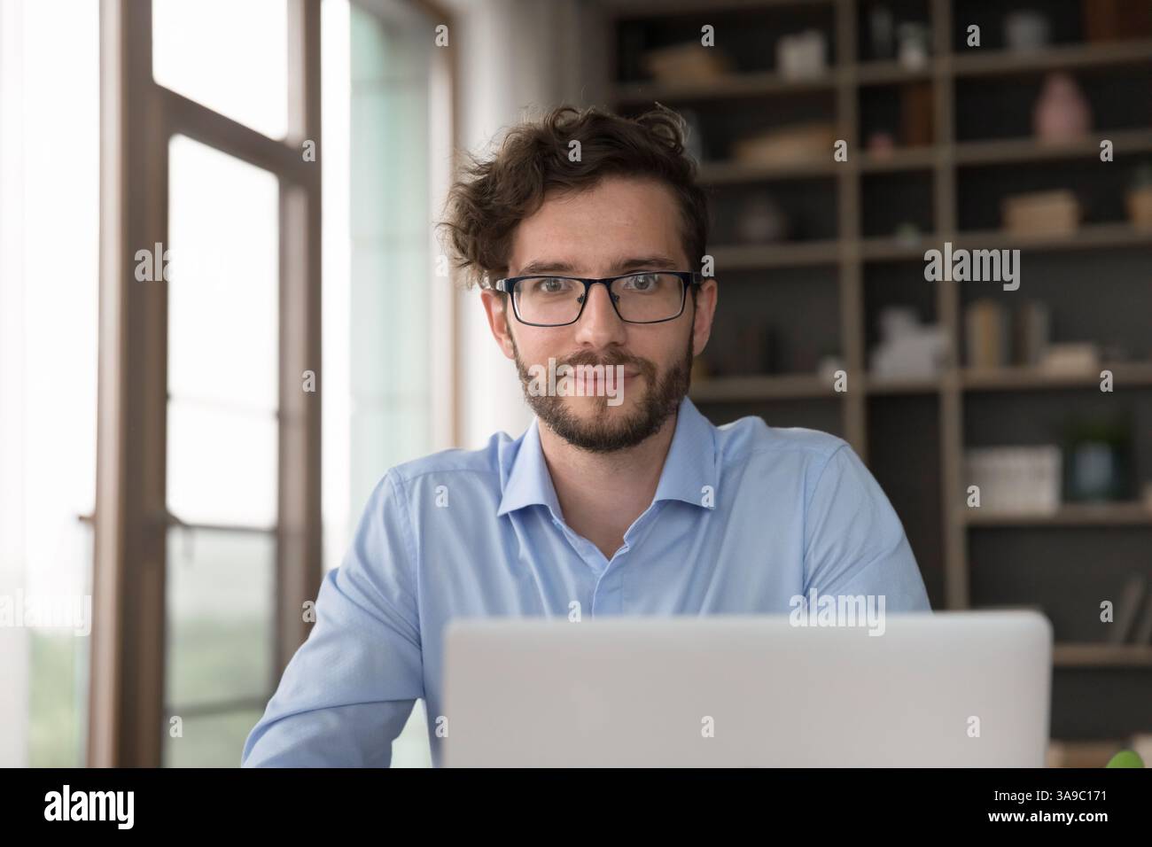 Happy millennial man worker look at camera above notebook screen Stock Photo