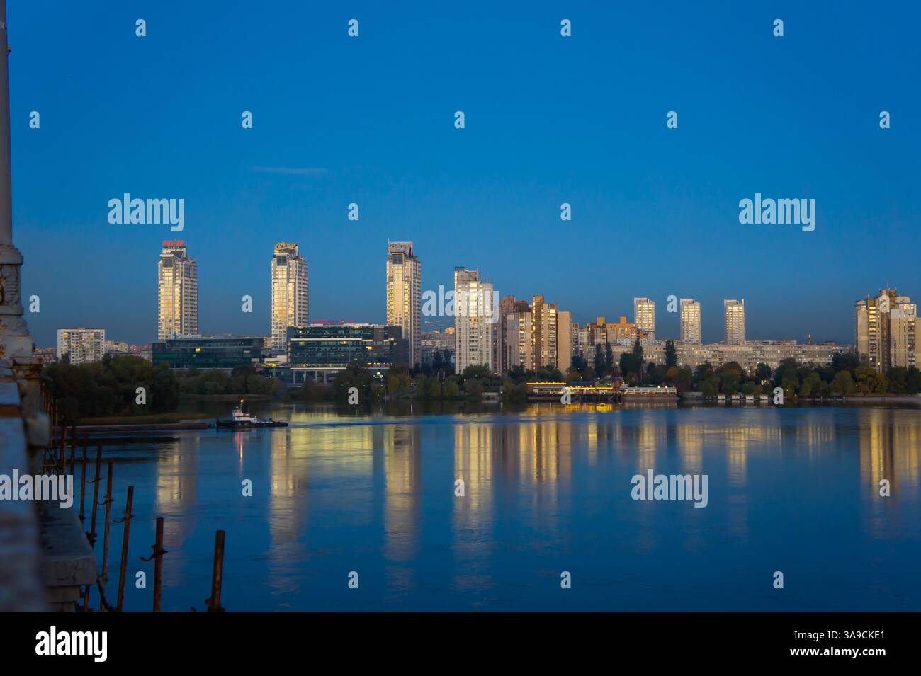 A modern cityscape at dusk with illuminated buildings reflecting on ...