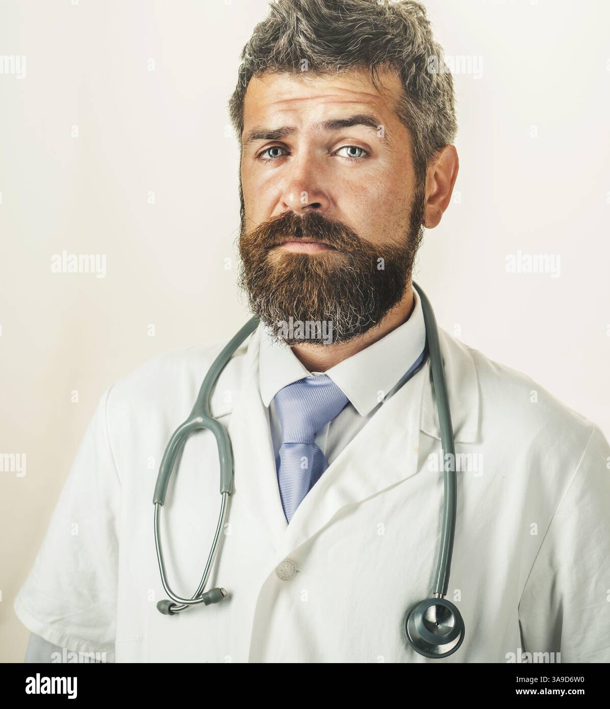 Portrait of serious doctor man with beard and mustache in medical gown with stethoscope. Medic profession. Bearded physician in white uniform with Stock Photo