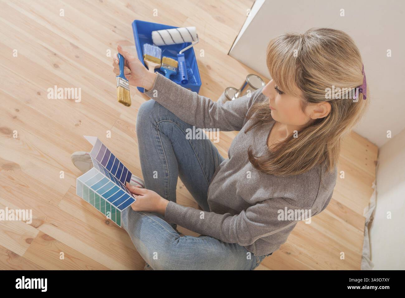 Female holding color palette and paintbrush and sitting on wooden floor ...