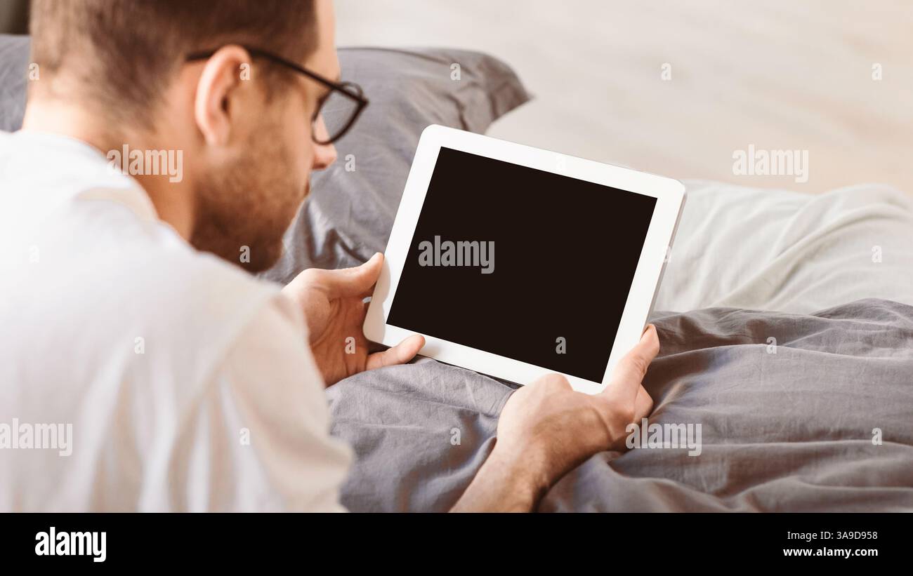 Man Using Digital Tablet With Empty Screen Lying In Bed Stock Photo