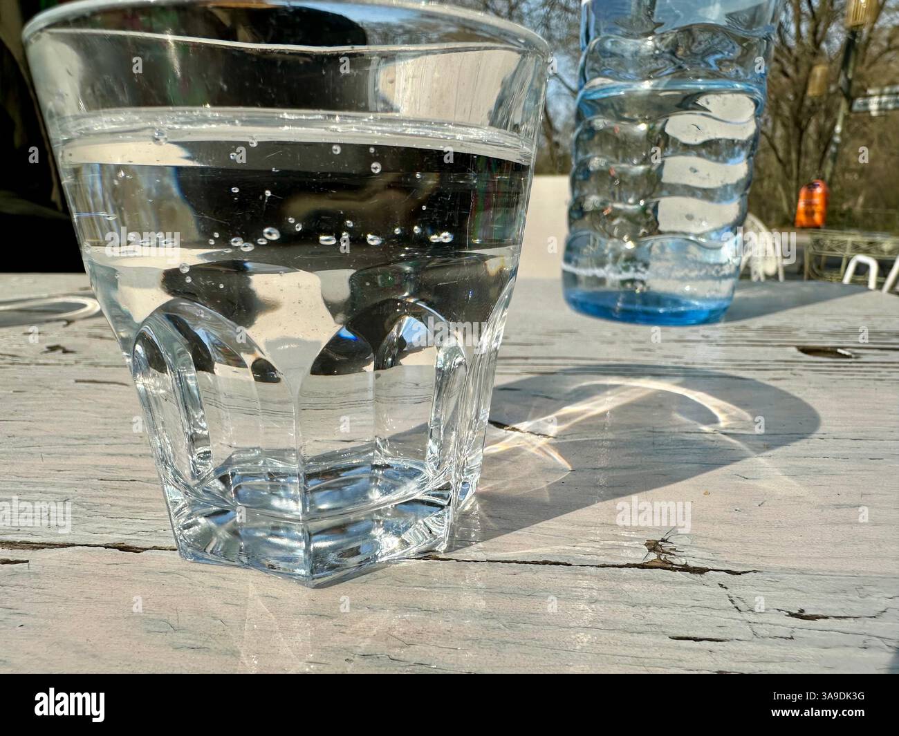 A close-up of a glass of sparkling water on a table outside with a water bottle in the background - Smartphone Captured Stock Image