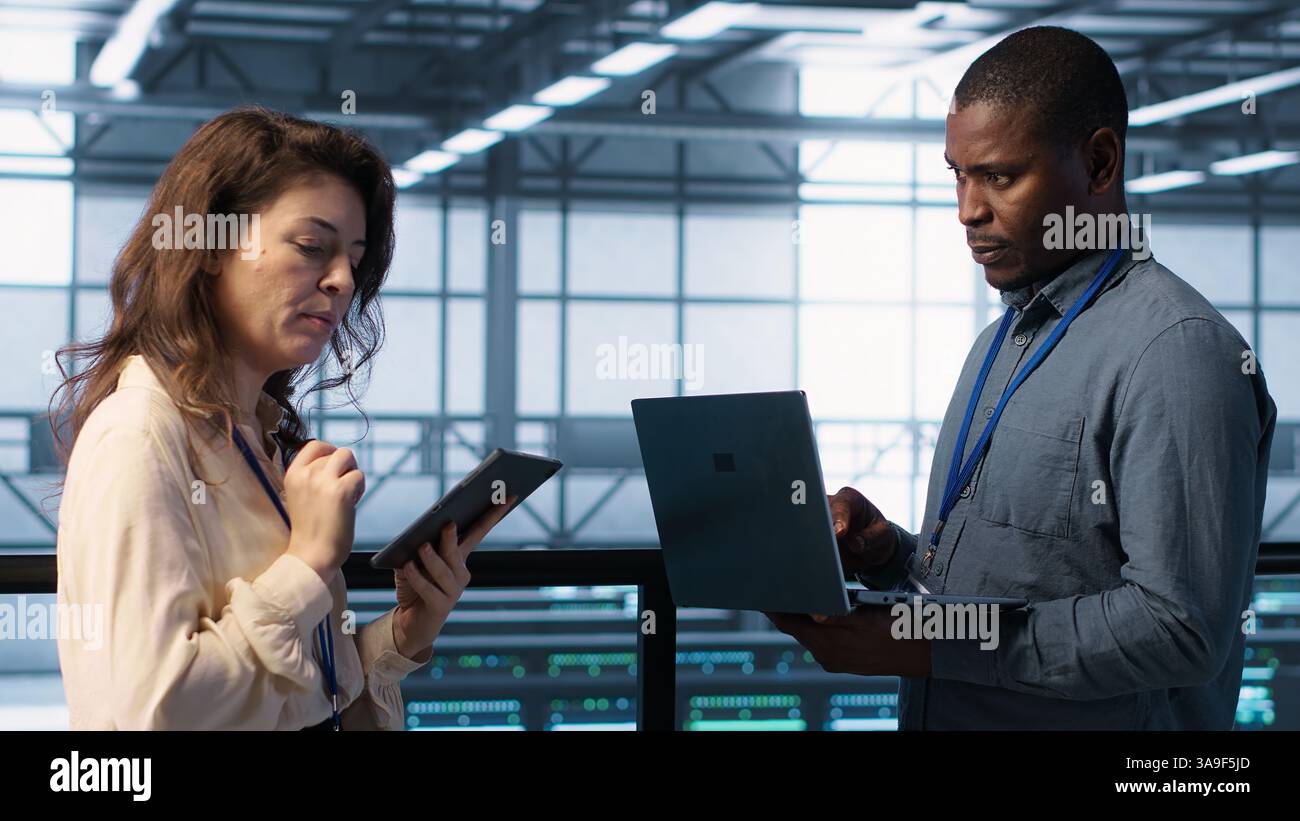 System administrators using notebook device in data center, managing server virtualization. IT specialists using laptop in server farm, sustaining long term infrastructure reliability, camera A Stock Photo