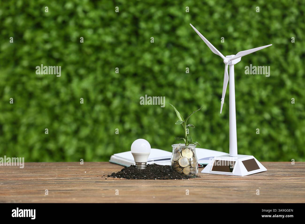 Wind turbine model with light bulb and coins on table outdoors. Green ...