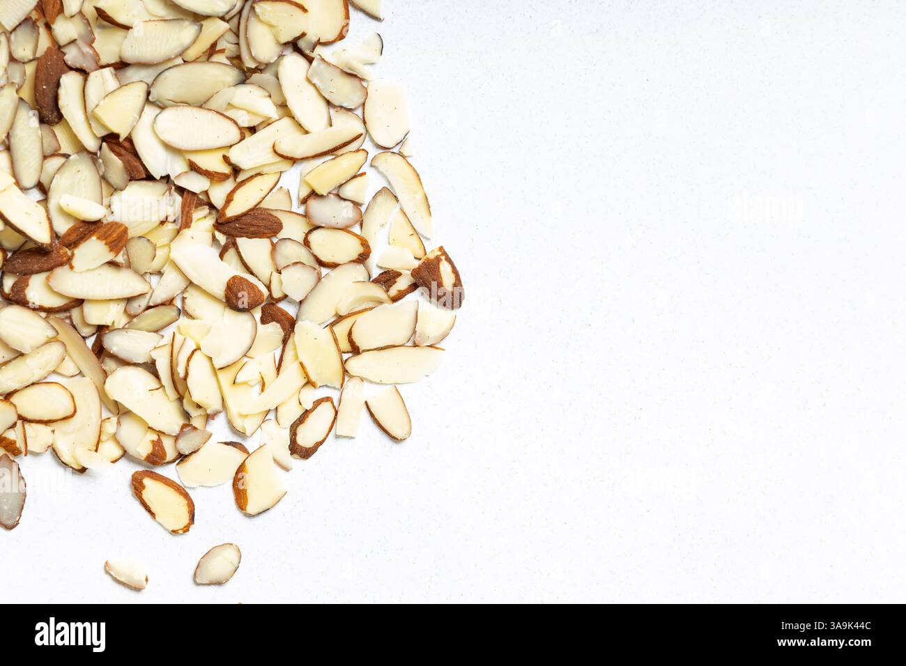 Sliced almonds scattered on a light surface in a kitchen setting, top view Stock Photo