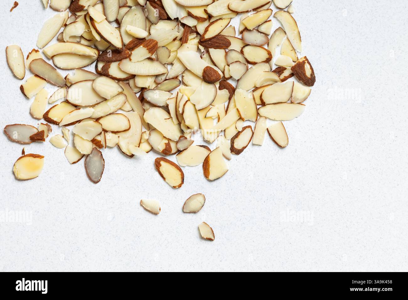 Sliced almonds scattered on a light surface in a kitchen setting, top view Stock Photo