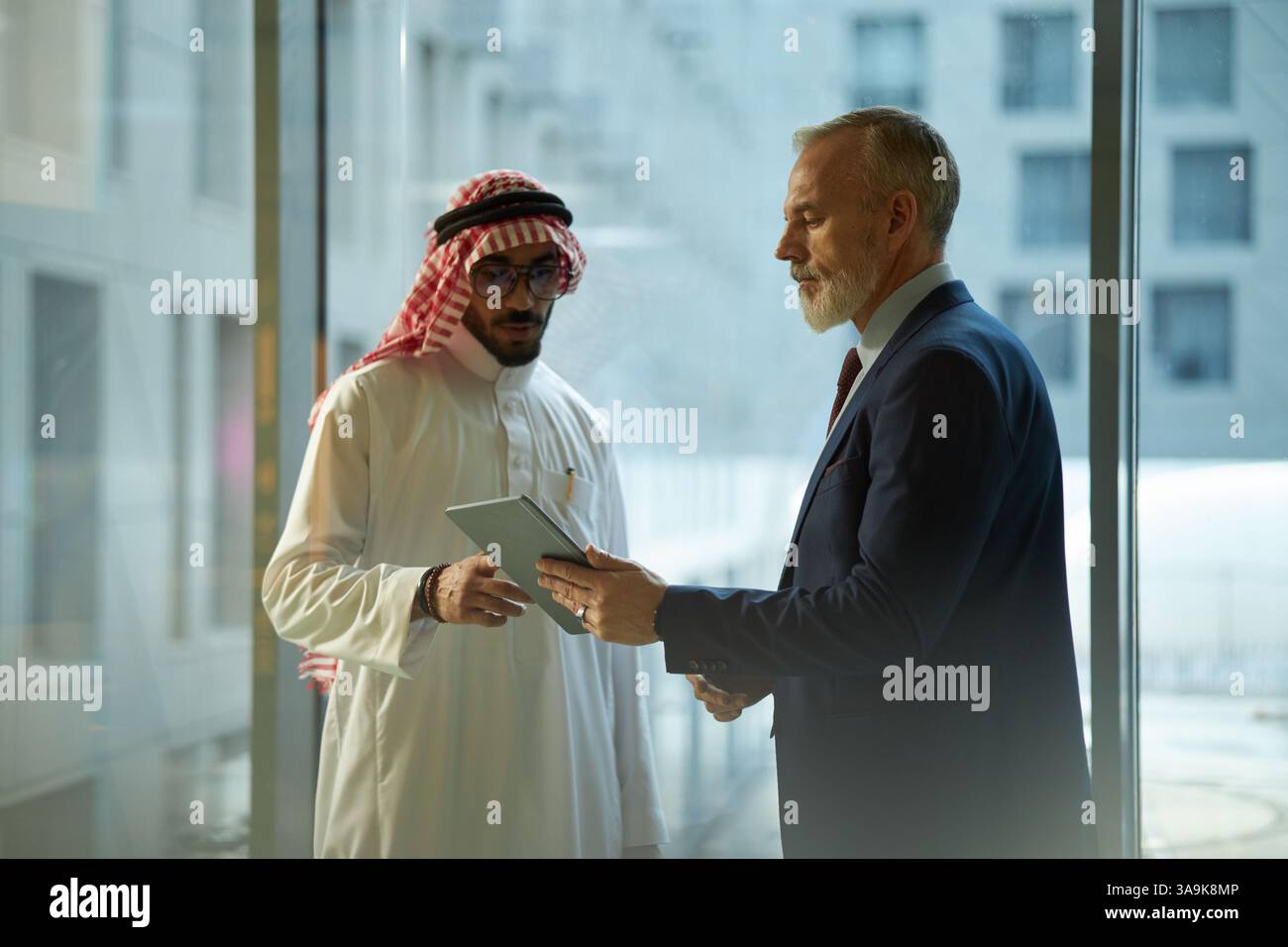 Young Middle Eastern and mature Caucasian businessmen standing in office, checking data on digital tablet Stock Photo