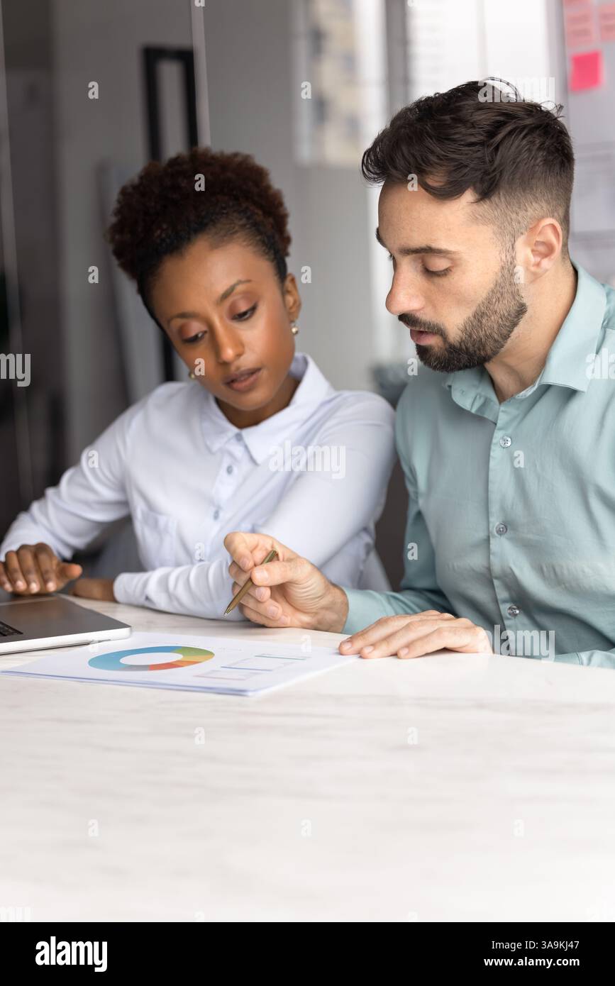 Two young diverse managers analyzing marketing report at office table Stock Photo