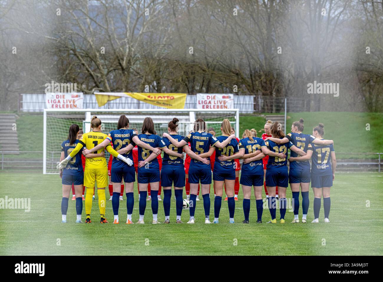 Andernachs Spielerinnen stehen während der Schweigeminute gemeinsam, Arm in Arm, auf dem Platz. Stock Photo
