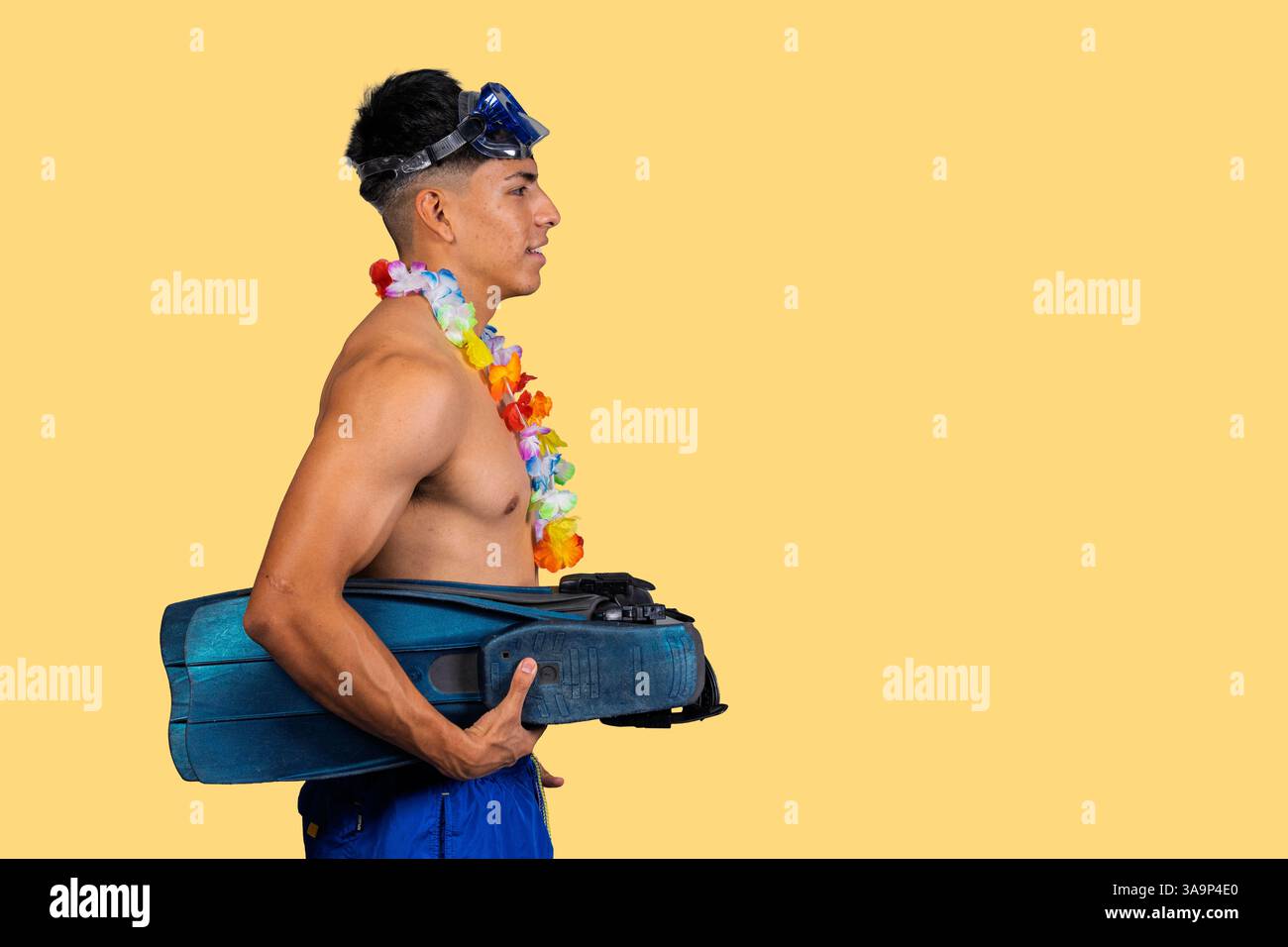Studio shot of a male tourist wearing a diving mask and lei holding flippers against a yellow background Stock Photo
