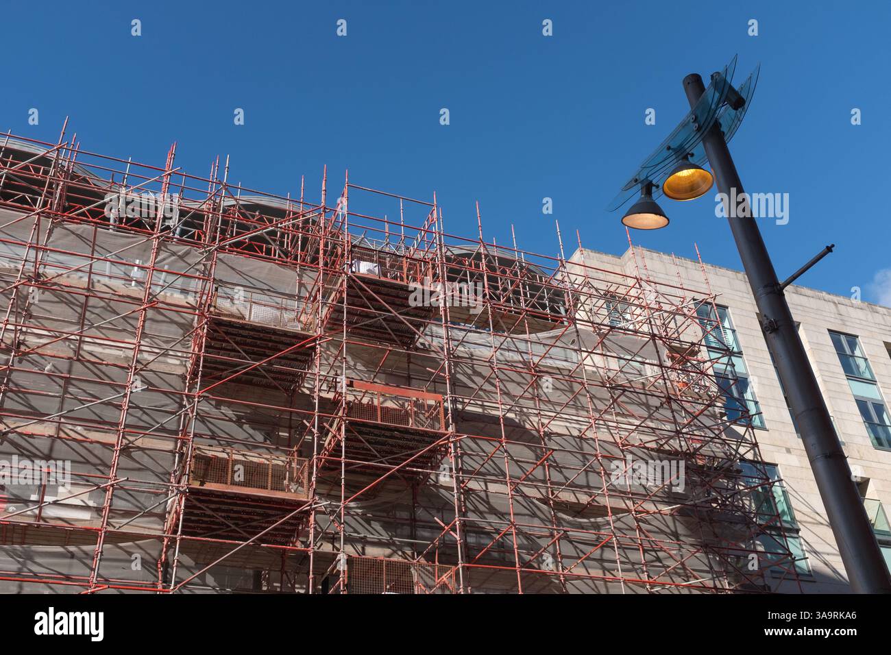 Looking up at scaffolding and construction work in Buchanan Street, Glasgow city centre, Scotland.  Street lighting stands out against the blue sky. Stock Photo