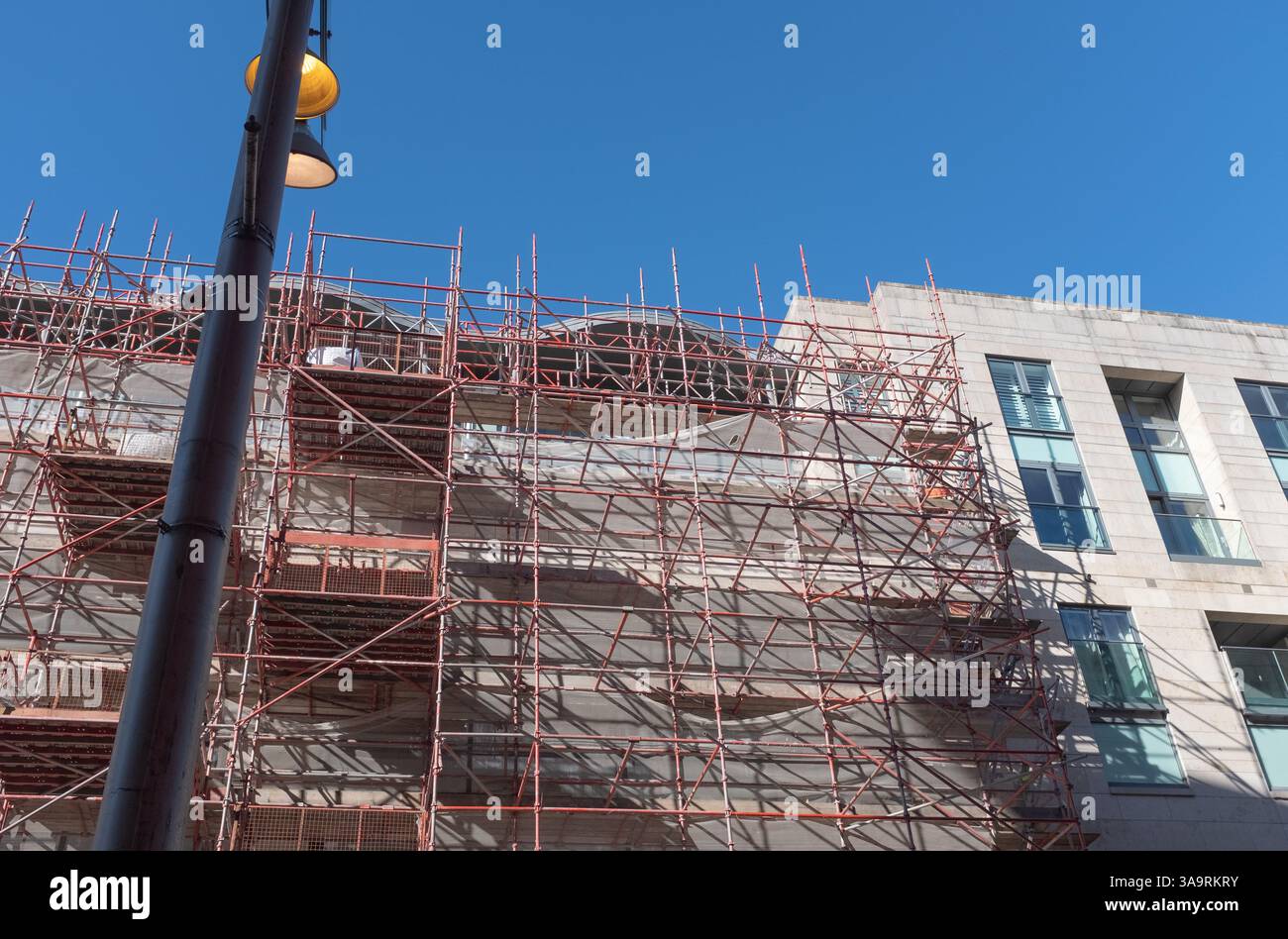 Looking up at scaffolding and construction work in Buchanan Street, Glasgow city centre, Scotland.  Street lighting stands out against blue sky. Stock Photo