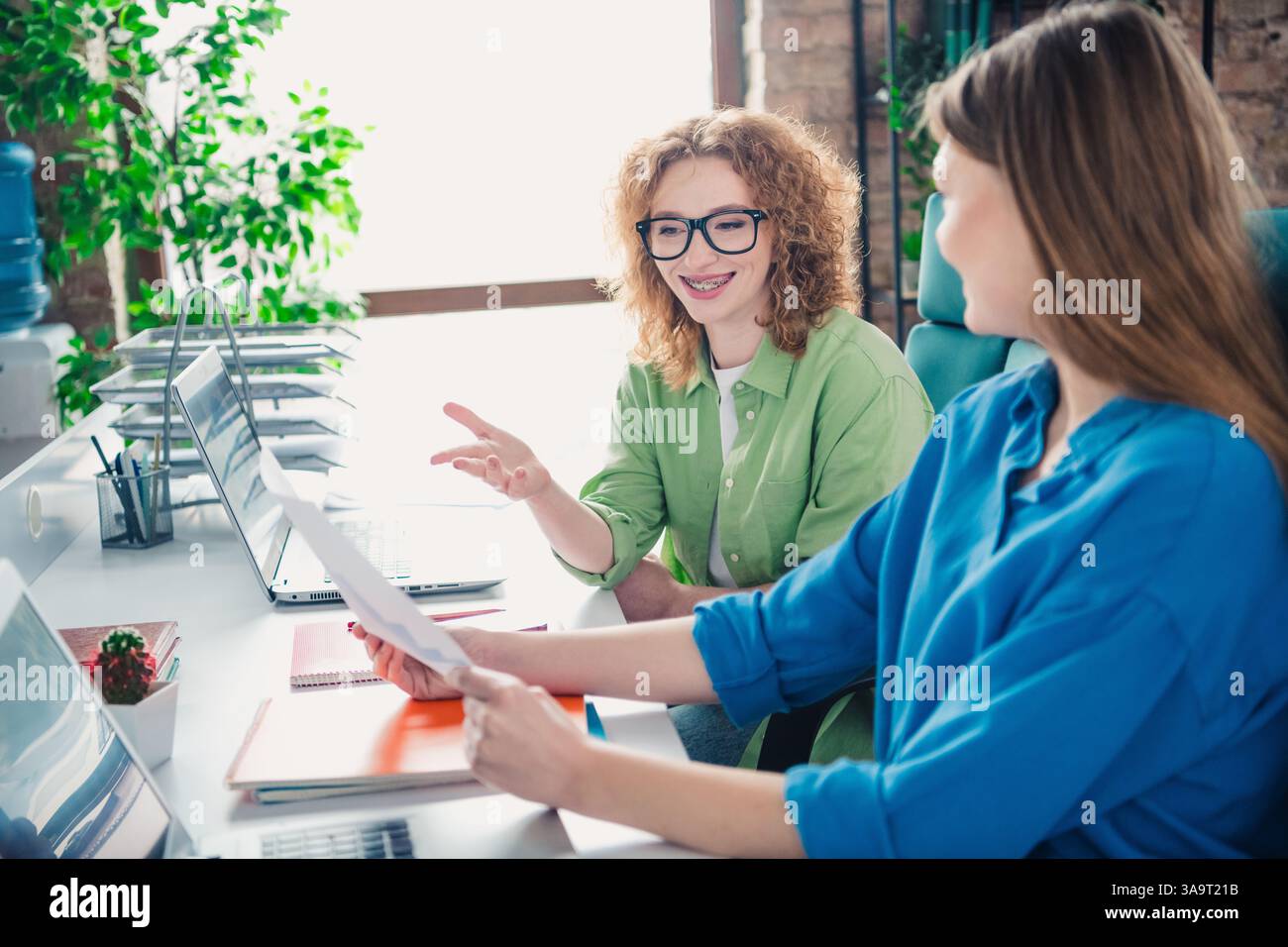 Two young professionals collaborating in a modern office setting with a ...