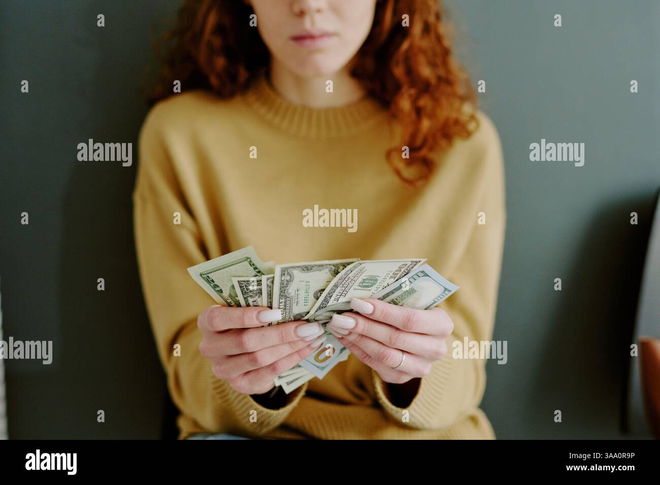 Person sitting down holding several dollar bills with both hands, intently focusing on counting cash, while wearing casual attire Stock Photo