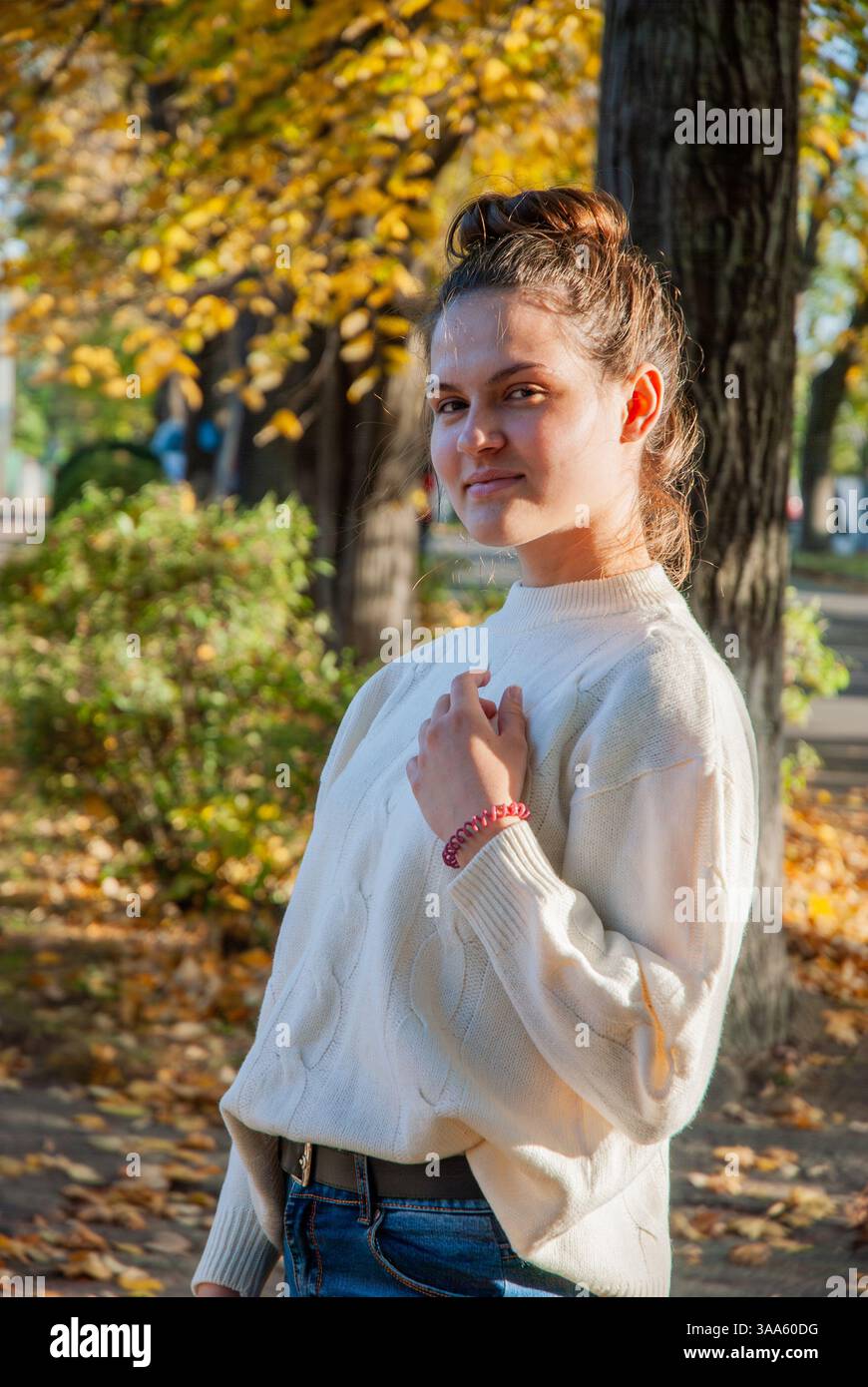 Autumn stroll in the park with young woman in cozy sweater and falling leaves. Stock Photo