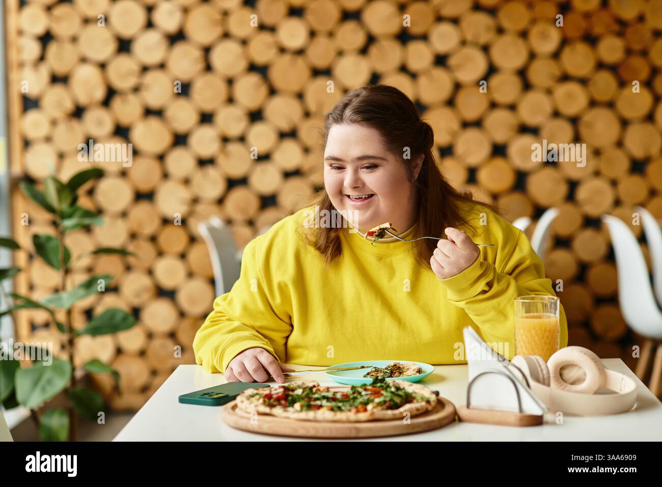 In a cozy cafe, a young woman with Down syndrome happily enjoys a tasty meal at her table. Stock Photo