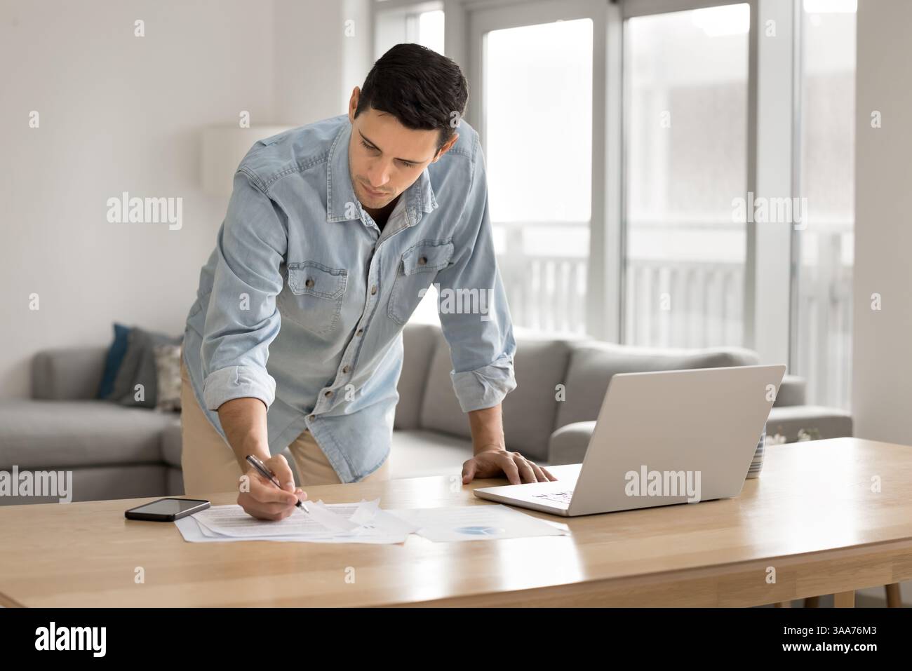 Man leaning over desk, making notes, focused on paperwork Stock Photo