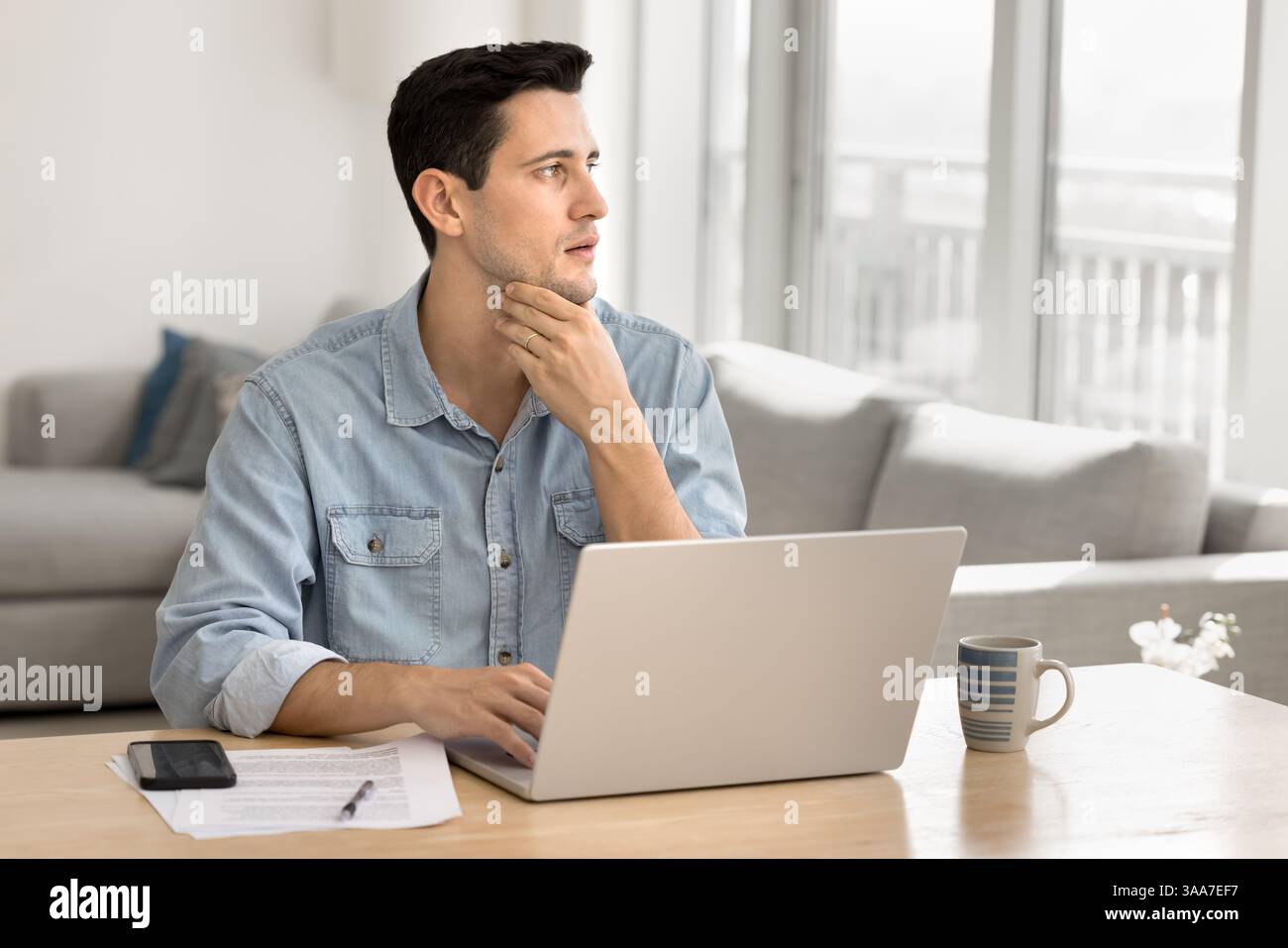 Man thinks, look aside while sit at desk with laptop Stock Photo