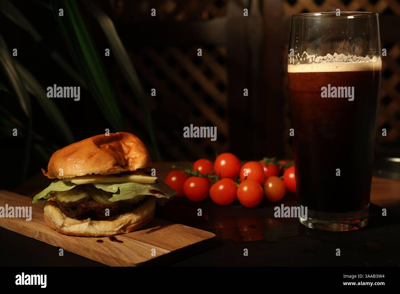 burger and glass of dark beer. video slow motion dark beer freshly brewed from a keg is poured into a glass. beef hamburger. restaurant. Stock Photo