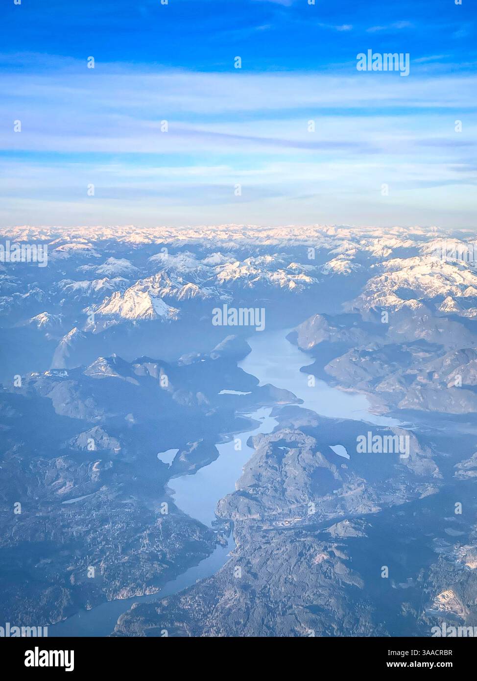 Aerial view showcasing snow-covered mountain peaks with winding lakes and rugged terrain below during flight. - Smartphone Captured Stock Image