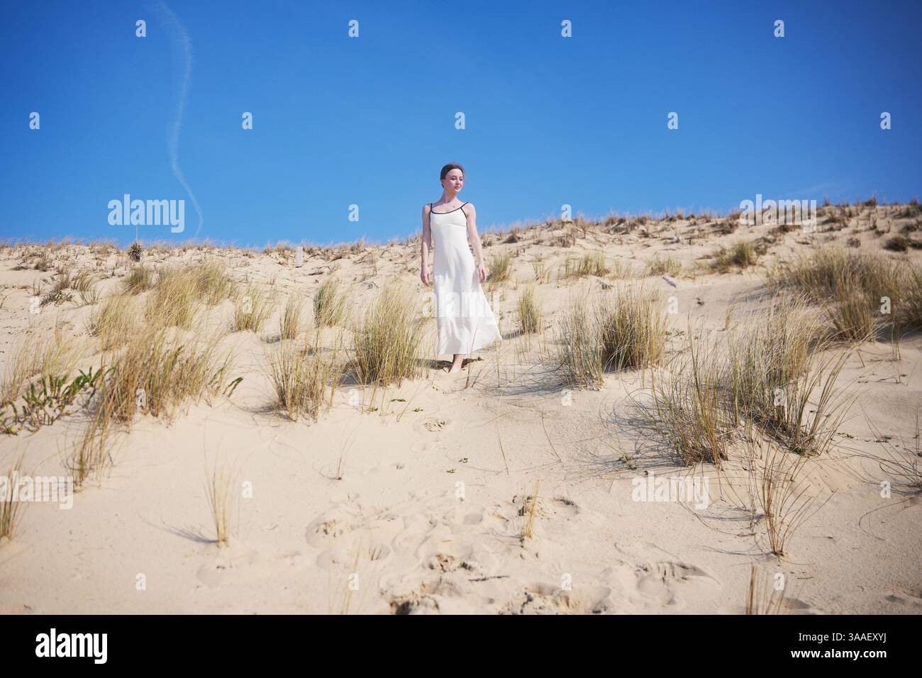 A barefoot woman in a flowing white dress walks peacefully down a sandy ...