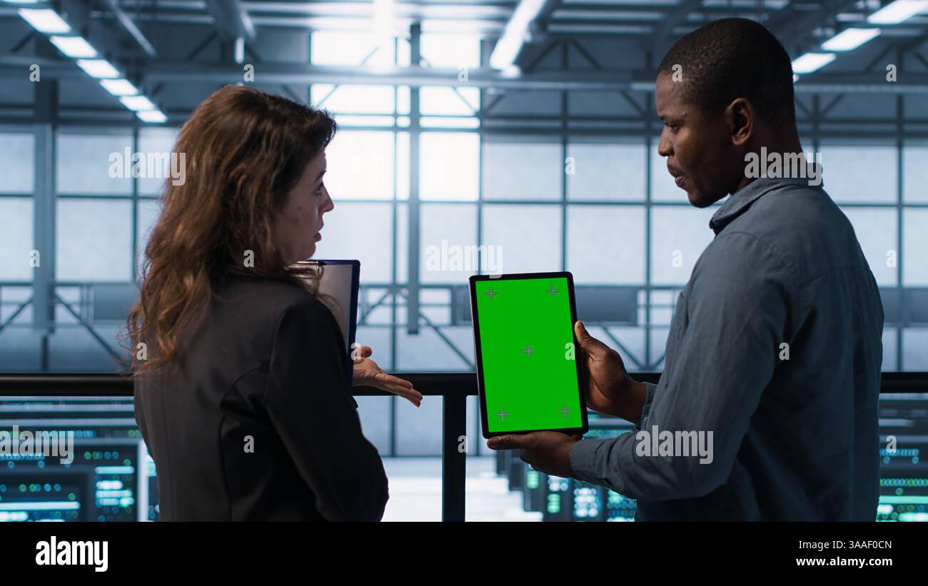 Software developers in data center using mockup tablet, observing performance analytics charts. Server hub IT professionals talking, using chroma key device, looking over graphs, camera A Stock Photo