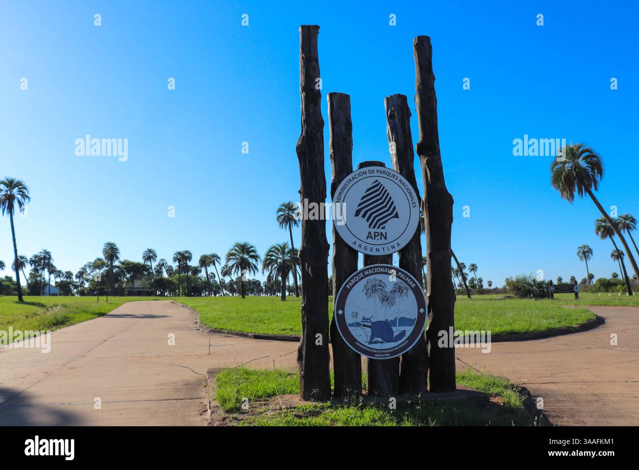 Entrance sign to El Palmar National Park, with text 'PARQUE NACIONAL EL PALMAR' in black letters on a white background. Clear blue sky and surrounding Stock Photo