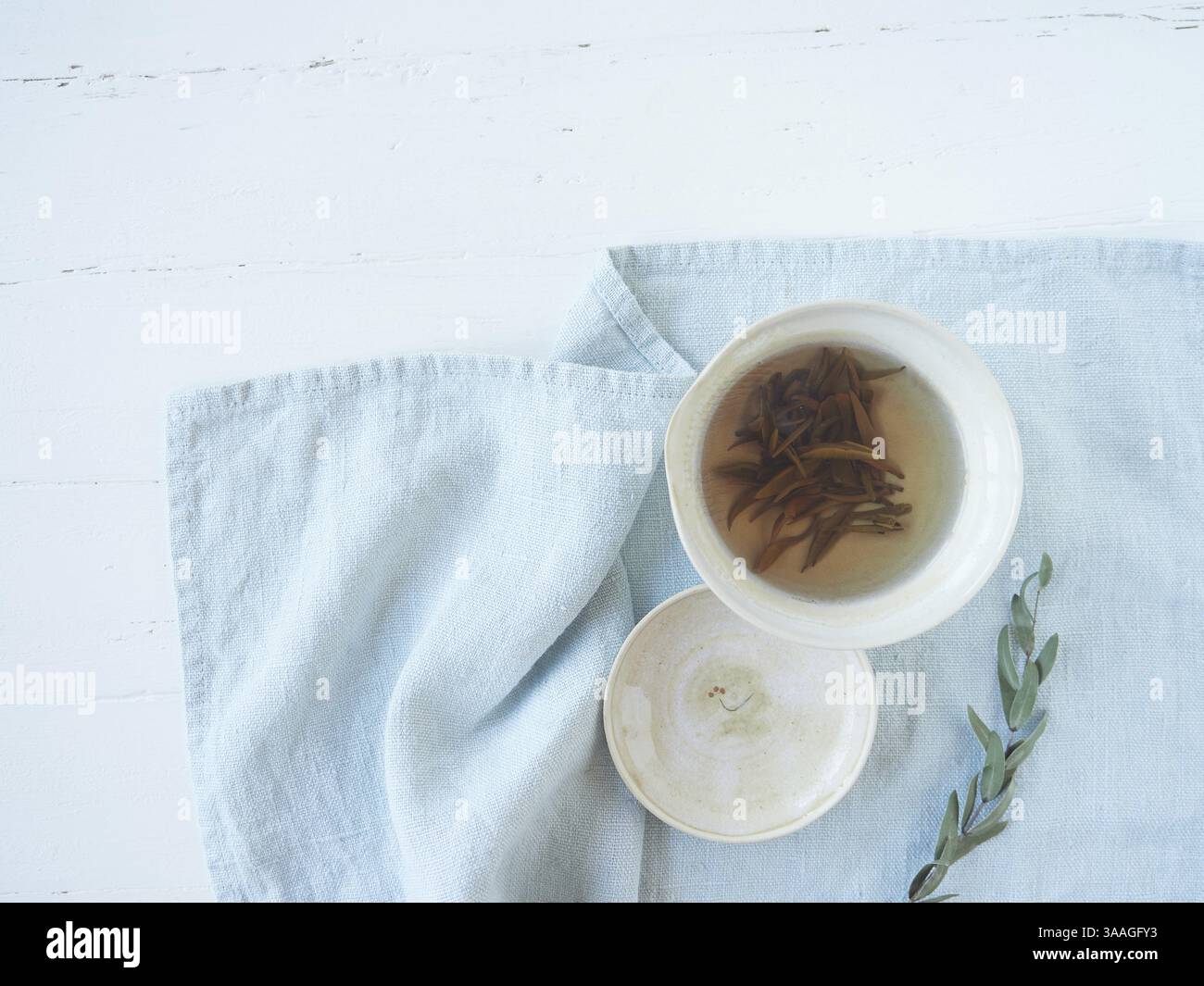 Beautiful traditional porcelain tea cup with Chinese white tea called silver needle or Bai Hao Yin Zhen. Leaf buds infused in hot water on blue cloth Stock Photo